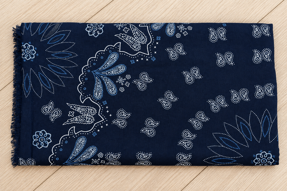 A navy blue bandana fabric with a white and light blue paisley pattern, laid flat on a light wood background.