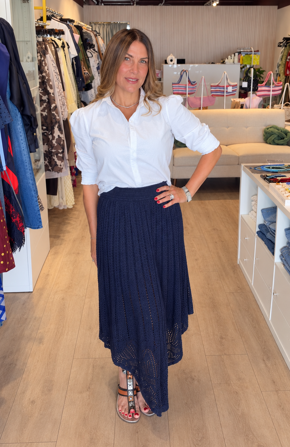 A woman modeling a white button-down shirt and a dark navy pleated midi skirt inside a clothing boutique.