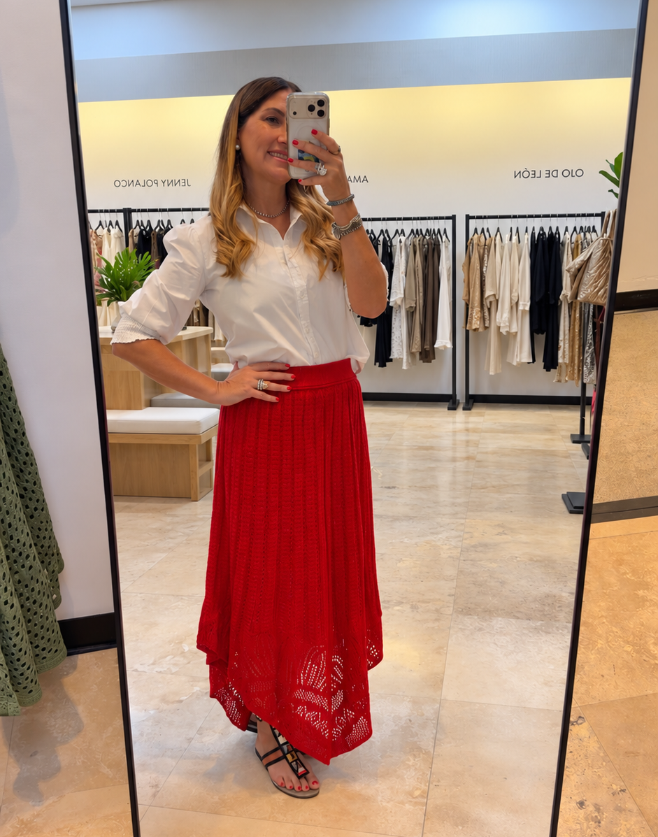 A woman takes a mirror selfie in a clothing store, wearing a white short-sleeve blouse and a high-waisted, pleated red maxi skirt with a lace overlay at the hem.