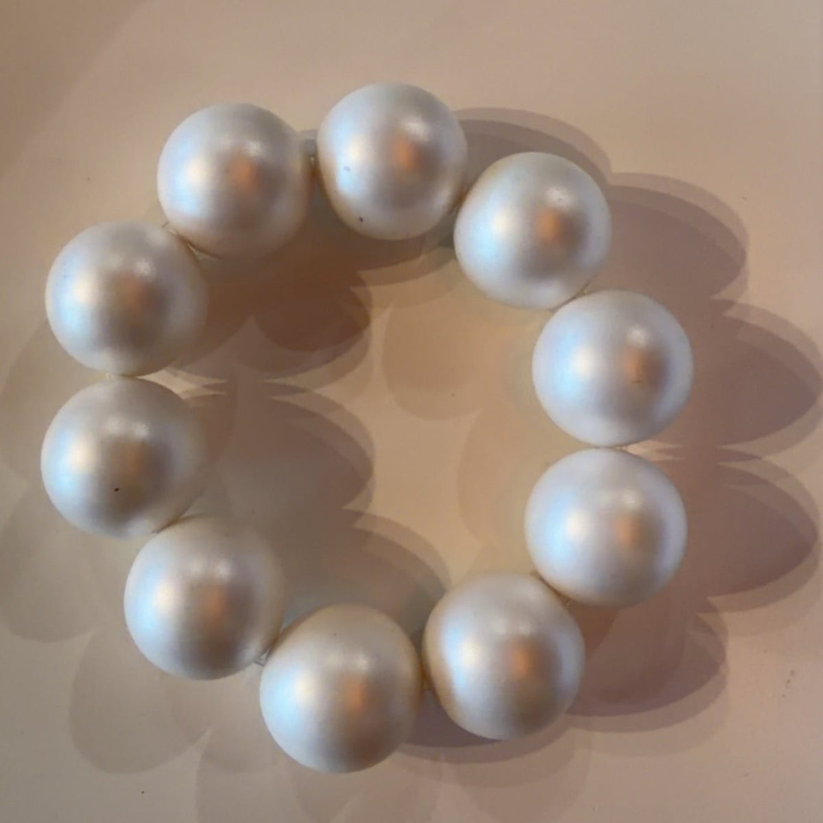 A bracelet made of large, glossy white pearls arranged in a circle on a light beige surface.