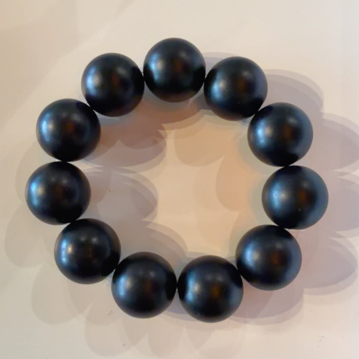 A beaded bracelet made of glossy, dark metallic spherical beads arranged in a circle on a light surface.