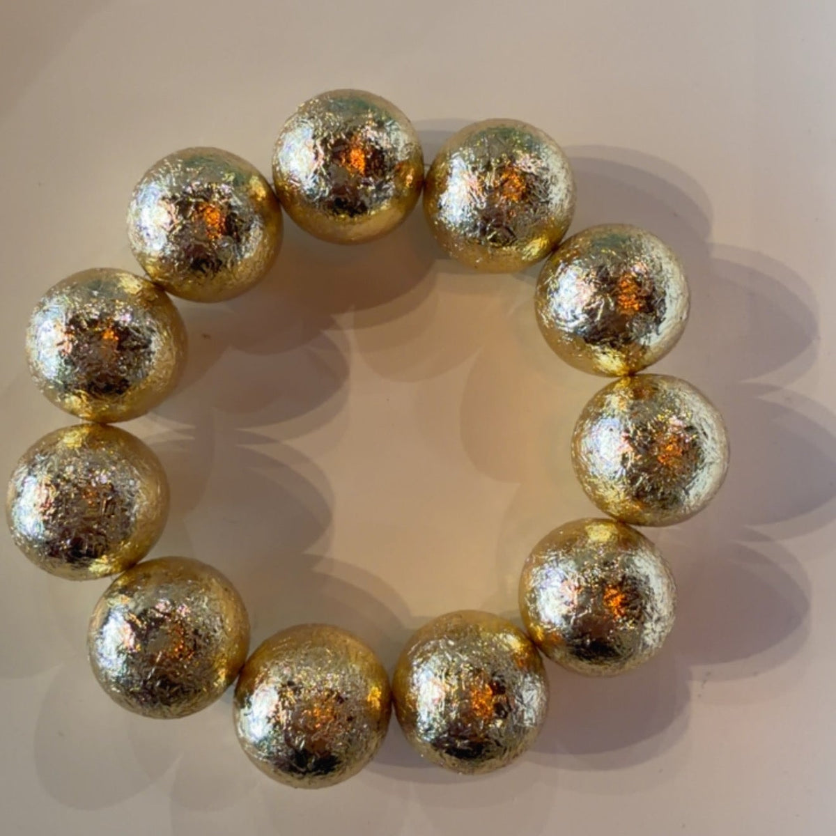 A beaded bracelet made of large, metallic gold marbled beads, arranged in a circle on a light beige background.
