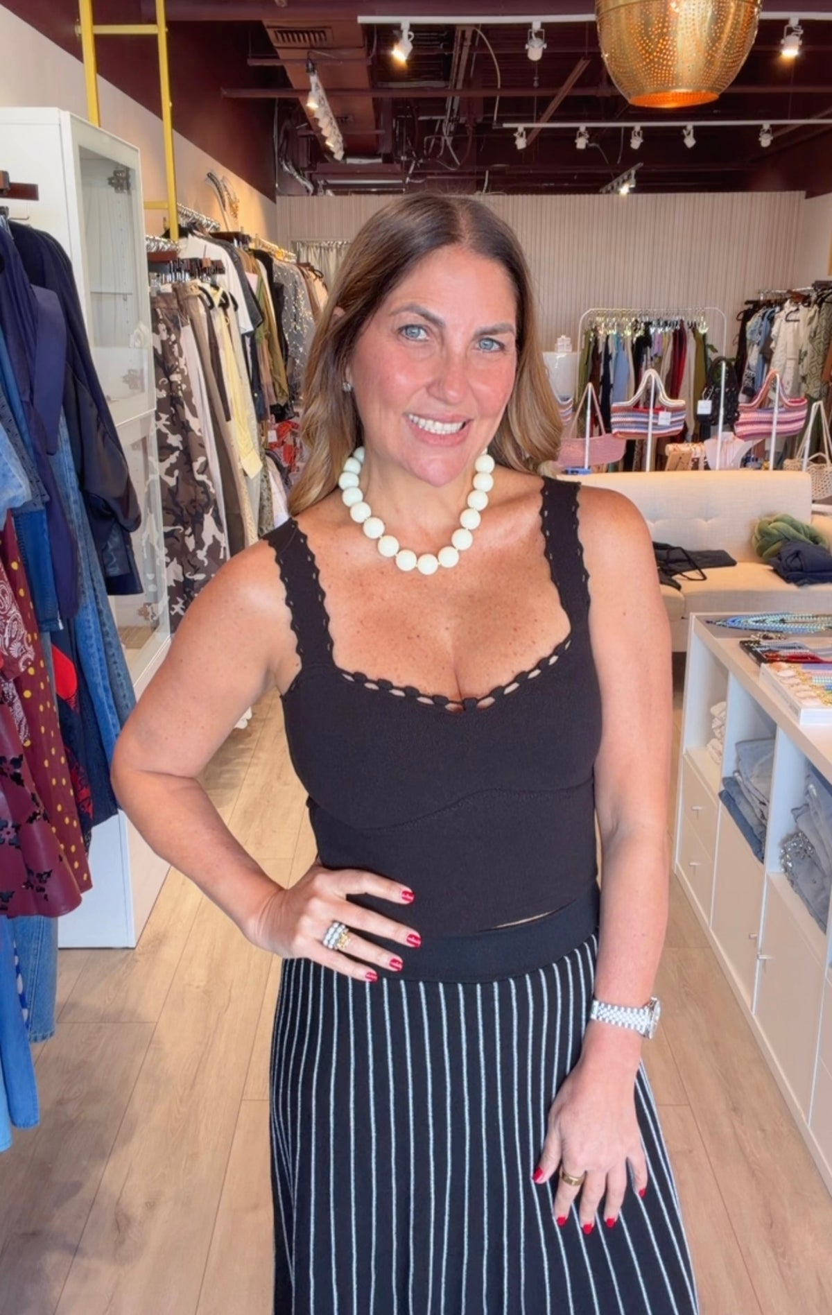 A woman modeling a black lace-trimmed tank top and a black and white vertically striped skirt inside a clothing boutique.
